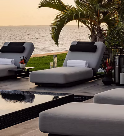 Poolside lounge chairs facing the ocean at sunset